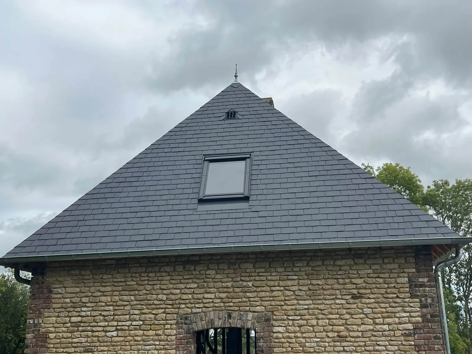 Toiture en ardoises naturelles avec fenêtre de toit et gouttière zinc sur une maison en pierre, couvreur à Bernay